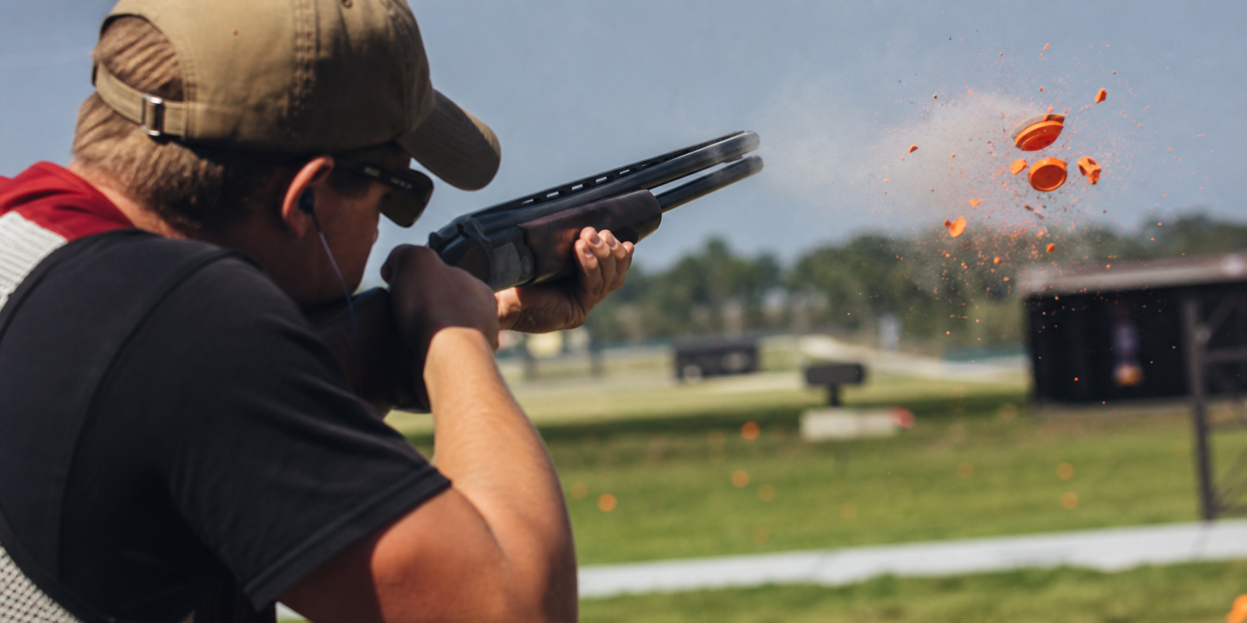 Shooter breaking an orange clay target in midair.